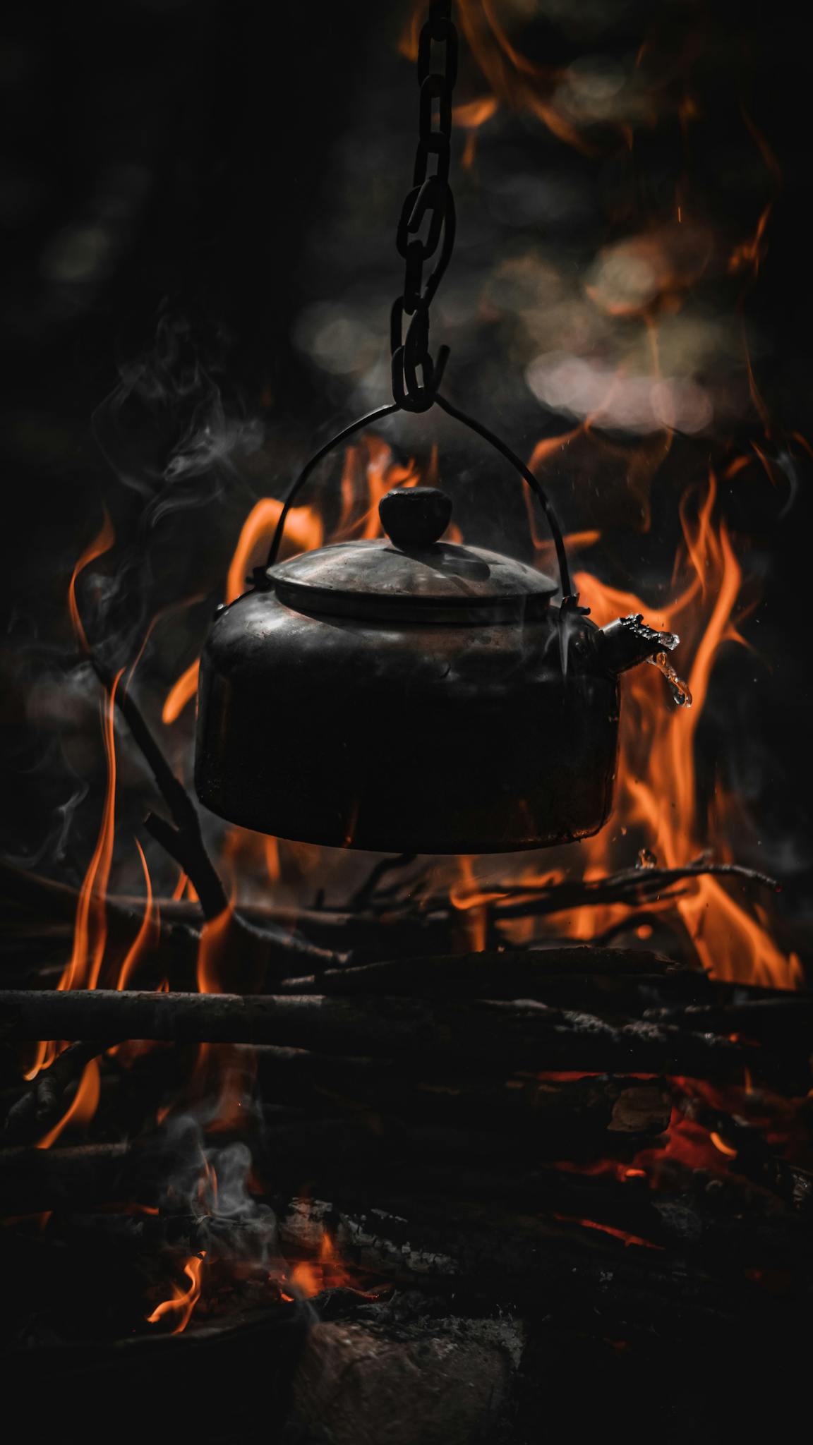 A black kettle hanging over a vibrant campfire in a forest setting, capturing the essence of outdoor cooking.