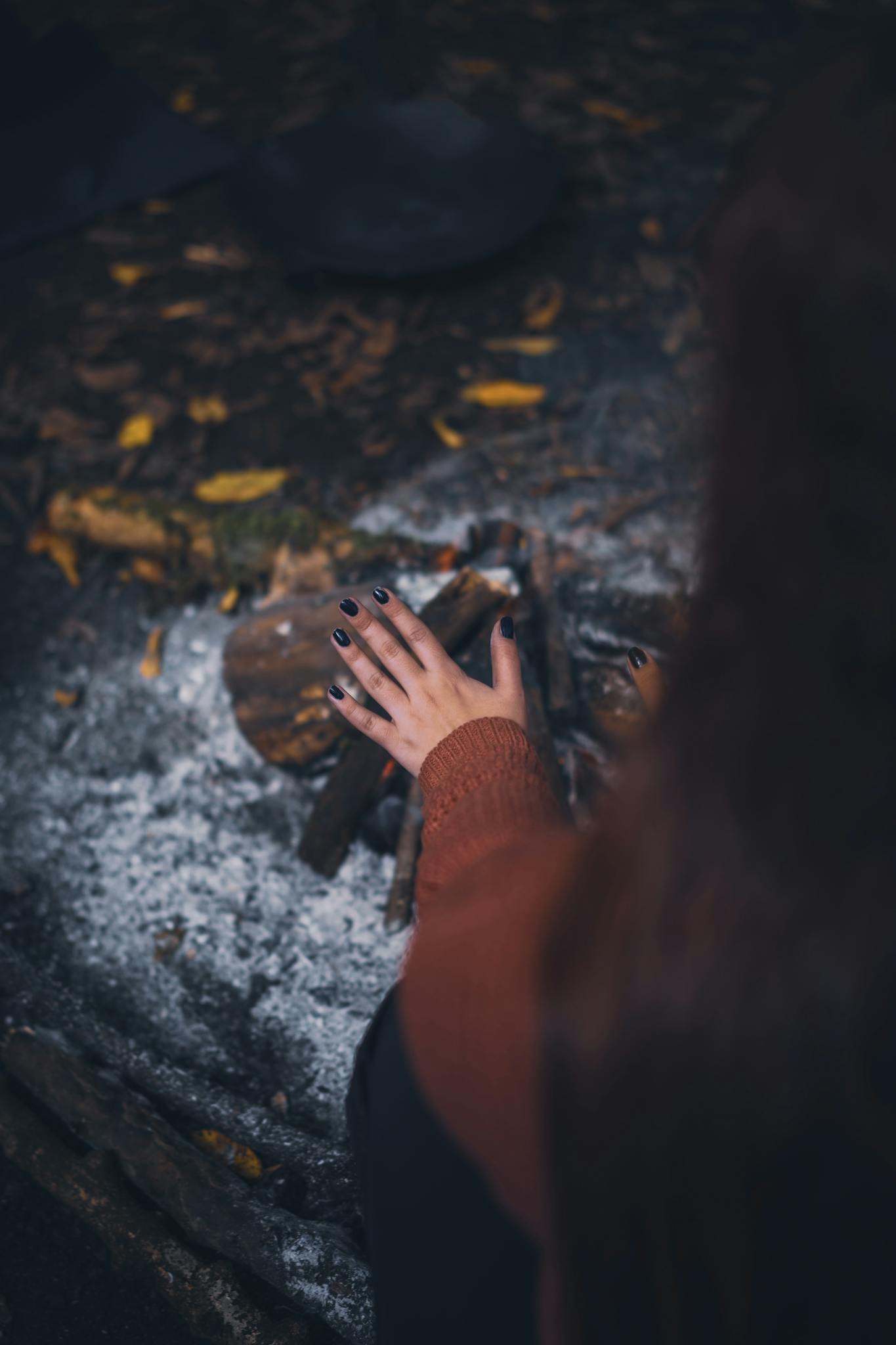 A person warming hands by a campfire in a cozy autumn forest setting.