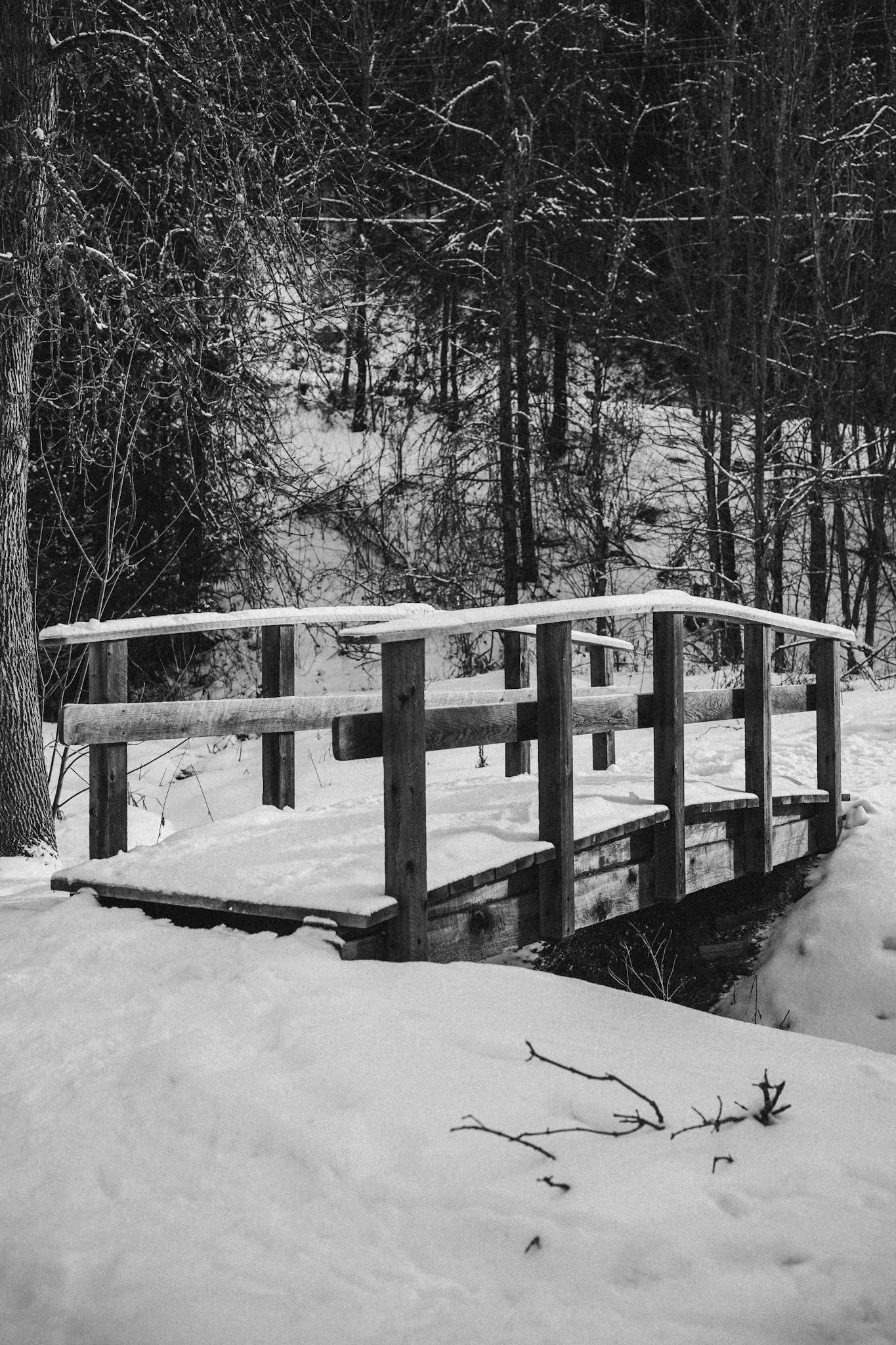 A rustic wooden bridge blanketed in snow amidst a serene winter forest scene