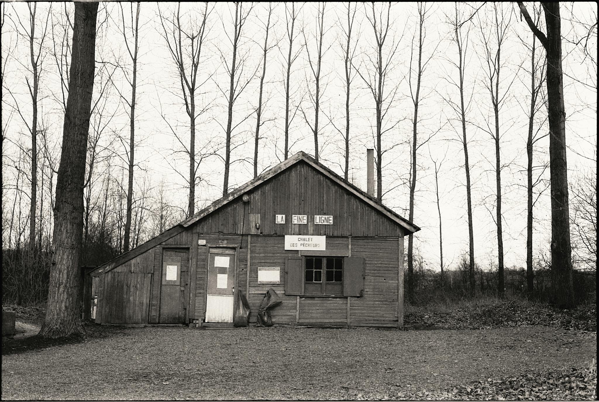 Black and white photo of a rustic cabin surrounded by leafless trees in winter.